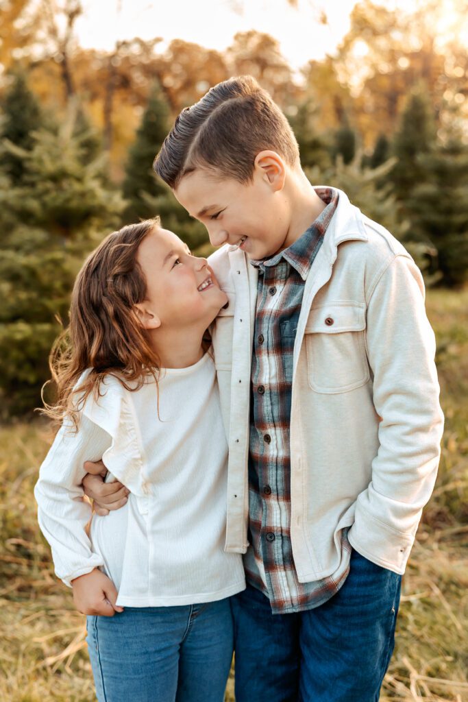 Brother and sister smiling at each other and hugging while outside at a sunset family photo session