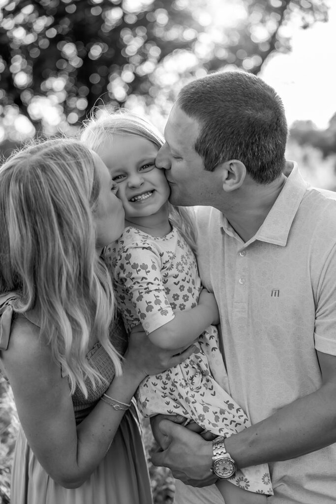 mom and dad kissing little girl on cheeks during family photos