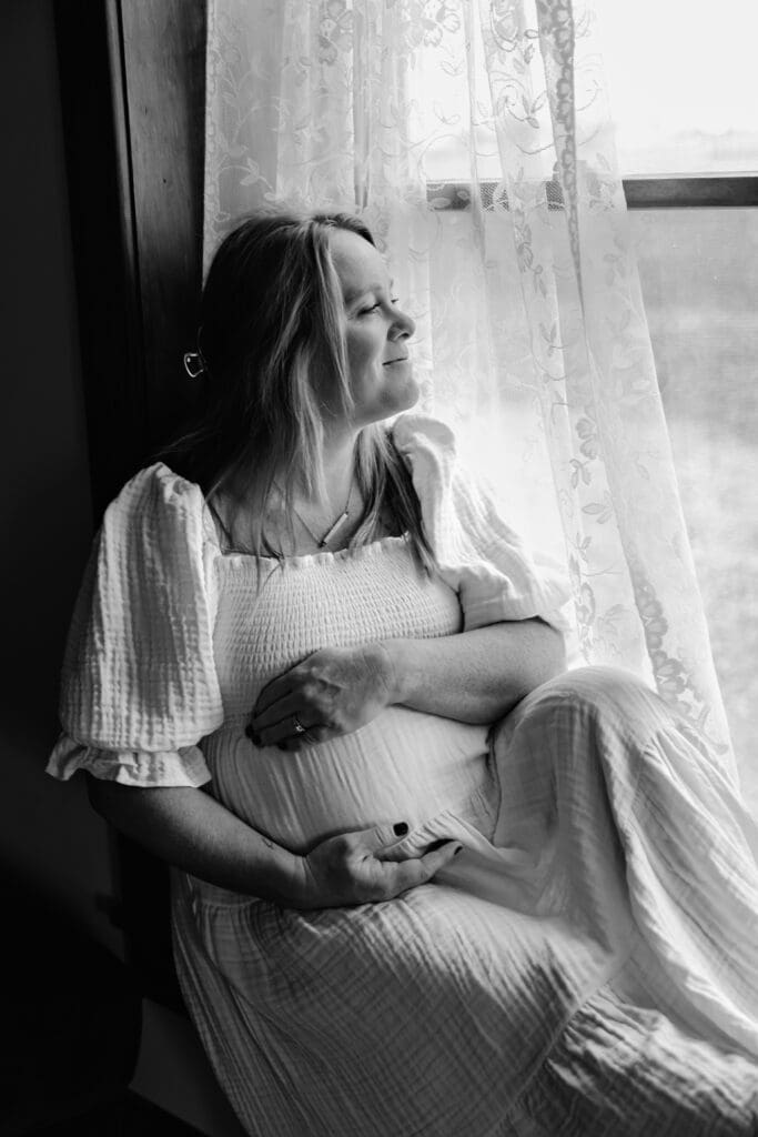 Maternity Session in client home with mom to be looking out window and holding belly