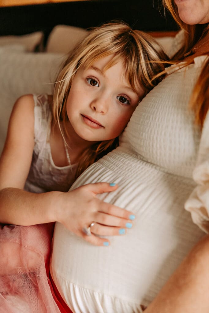 Little girl leaning into mom's belly during maternity photos