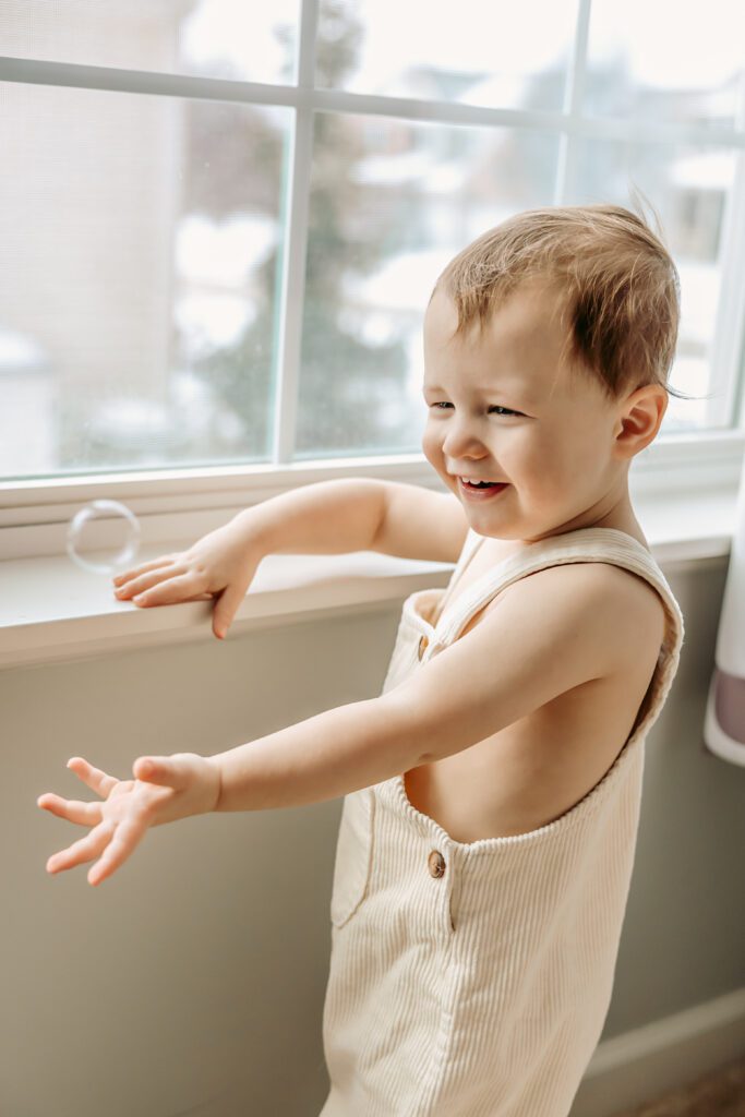 Toddler smiling and reaching out at bubble blown during a fun milestone photo shoot