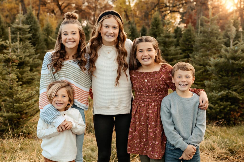 5 kids smiling for a photo among the christmas trees at tree farm photo sessions