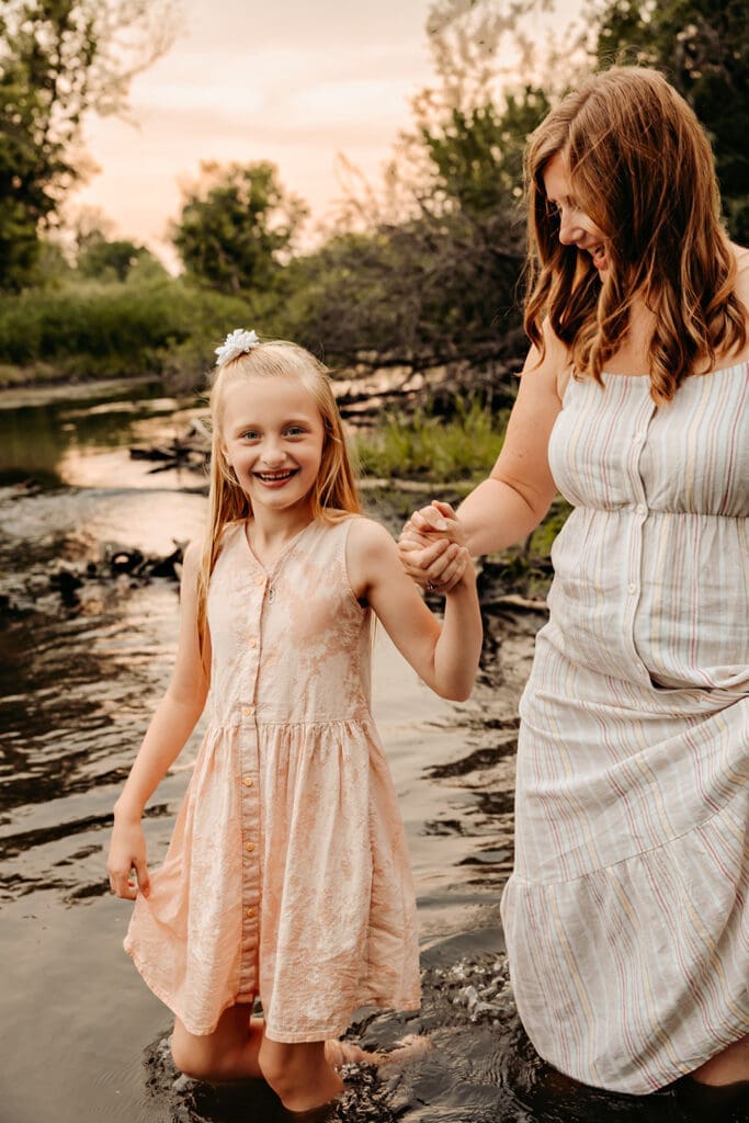 Mom holding daughters hand and standing in the creek during summer family photos
