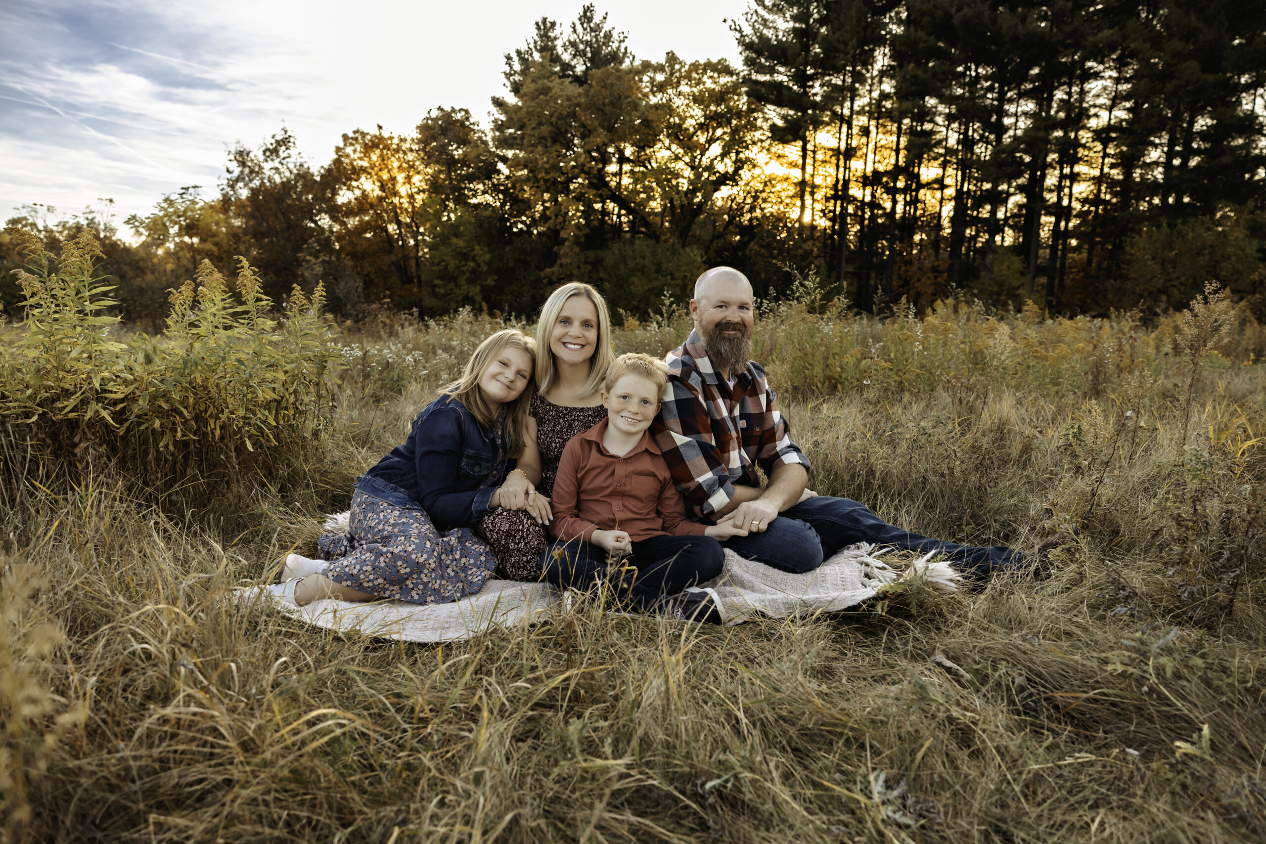 Family of 4 sits together in a field during fall family photos in mchenry county